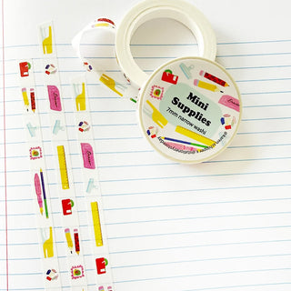 A roll of washi tape featuring colorful school supply illustrations, displayed on a lined notebook page.