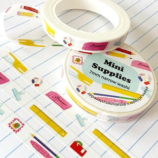 Washi tape featuring a school supplies (pencil, ruler, clip, stamp, etc) pattern, displayed on a white background with blue lined paper.