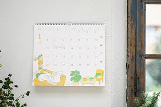 Wall calendar with a design of two dogs on a couch hanging on a wall.