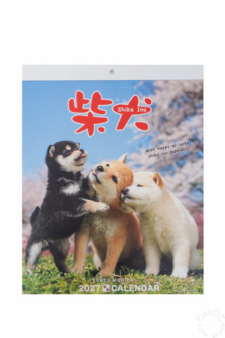 A 2027 Shiba Inu wall calendar featuring three puppy dogs outdoors under cherry blossoms, with large red Japanese characters