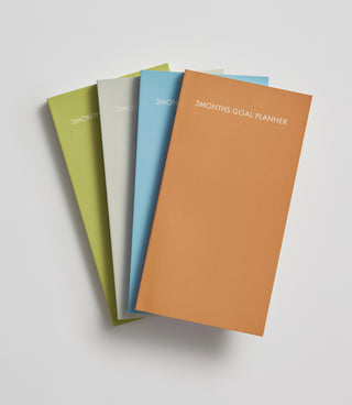 Four goal planners in different colors on a light gray background
