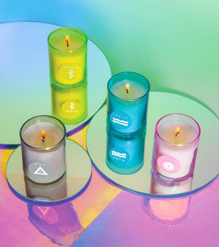 Four colorful candles in transparent holders on a reflective surface with a gradient background.