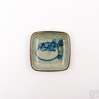 Square ceramic dish with blue puffer-fish face illustration, speckled aqua glaze