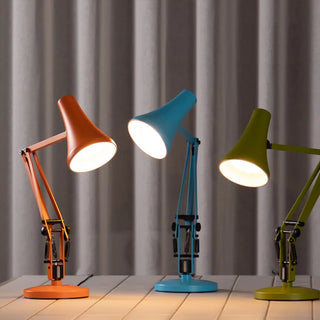 Three colorful desk lamps on a tile surface with a gray curtain background