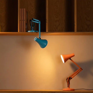 Two adjustable desk lamps, one blue and one orange, on a wooden surface with a wooden panel background.