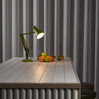 Green desk lamp on a tile table with fruits against a gray curtain background