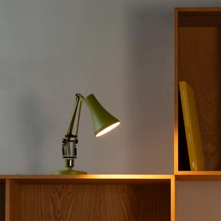 Green desk lamp on a wooden surface with a gray wall and bookshelf in the background