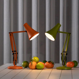 Two desk lamps, one orange and one green, on a tile surface with fruits.