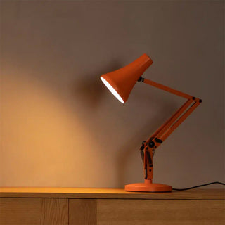 Orange desk lamp on a wooden surface with a warm glow against a dark background