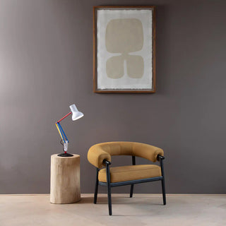 Modern chair with a side table and lamp against a gray wall with a framed abstract painting.