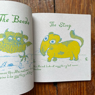 Open book with illustrations of a green creature and a yellow elephant-like character on a wooden surface.