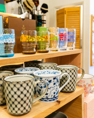 Collection of patterned mugs on a wooden shelf with a store interior background.