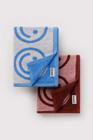 Folded set of baggu hand towels with smiley face pattern. one in red and pink colorway and other in blue and white colorway