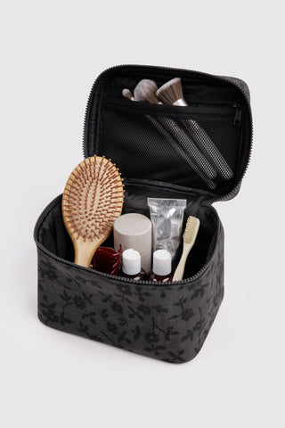 cosmetic case with handle in black floral pattern opened with various beauty products inside
