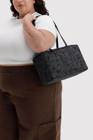 person wearing baggu medium bowler bag in black floral pattern on their shoulder