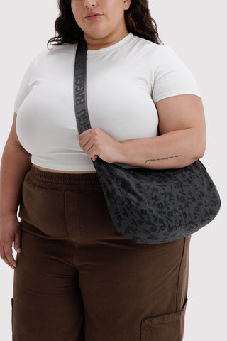 person wearing baggu medium crescent bag in black floral pattern across their body