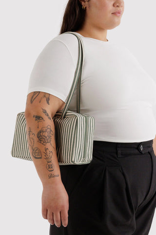 Person wearing a white shirt and black pants with a green and white striped bag over one shoulder on a white background