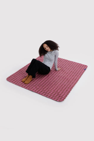 person sitting on baggu puffy picnic blanket in a pink tartan pattern