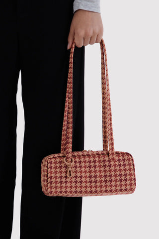 person holding small bowler bag in tan houndstooth pattern in their hand