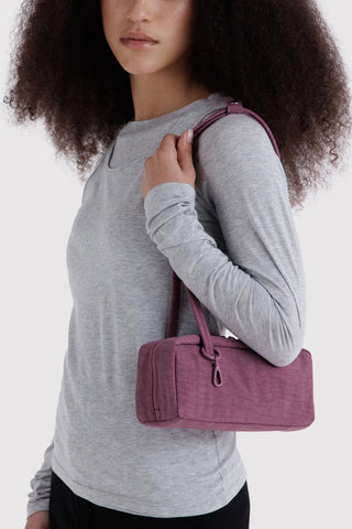 person wearing gray shirt and holding small nylon bowler bag in plum on their shoulder