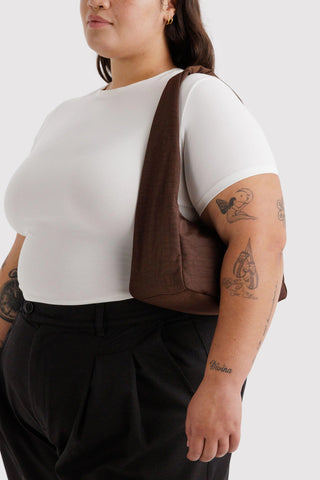 Person wearing a white t-shirt and black pants with a brown bag over one shoulder on a white background