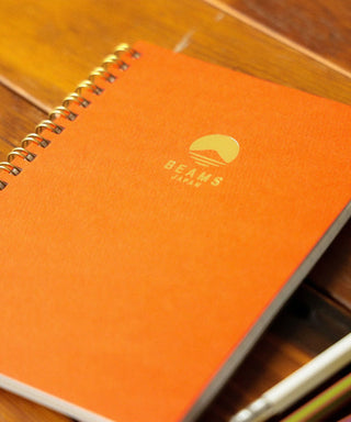 Orange notebook with Beams logo on a wooden surface