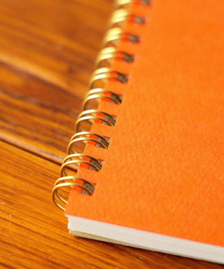 Orange notebook with gold spiral binding on a wooden surface