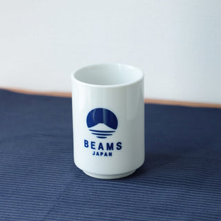 White mug with blue 'BEAMS JAPAN' logo on a blue textured surface