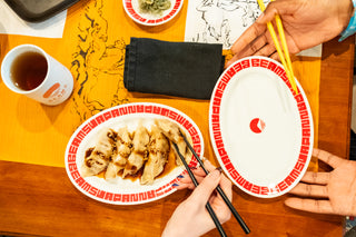 Dinner scene with dumplings on a plate, chopsticks, and a cup of tea on a table with decorative tablecloth