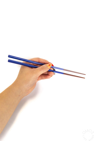 Hand holding blue chopsticks on a white background