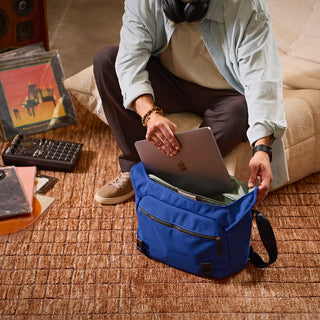 Person sitting on a couch putting a laptop in a blue messenger bag in a living room setting