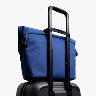Blue bag with its strap around a luggage handle to be a carry on bag on a white background