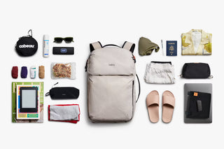 Collection of travel items arranged around a backpack on a white background