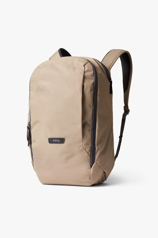 A beige backpack with gray accents, featuring a small brand label on the front, on a white background.