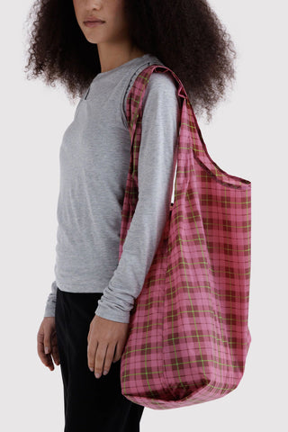 person wearing big pink and green tartan patterned baggu tote bag on their shoulder