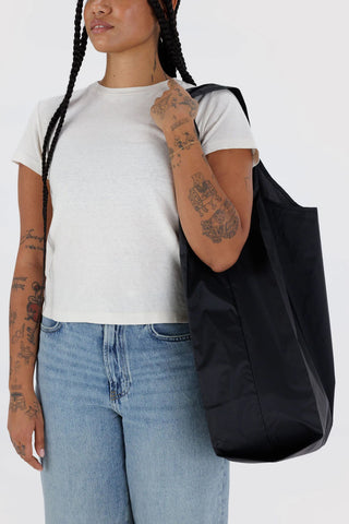 person in t-shirt and jeans holding large black baggu tote on their shoulder