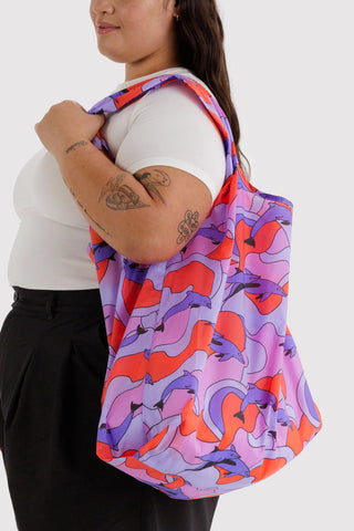 Person holding a colorful tote bag with dolphin patterns on a white background