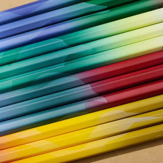 A close-up diagonal arrangement of colorful pencils in blue, green, yellow, red, and orange on a tan background.