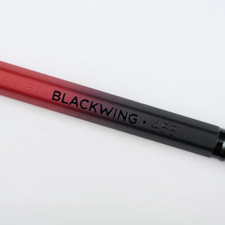 A close-up of a pencil showing a color gradient from red to black, with the text 'BLACKWING 458' printed on the barrel.