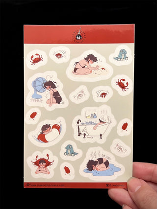 Sheet of stickers with various illustrations held by a hand against a dark background
