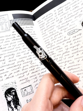 Hand holding a black pen over a notebook with writing and illustrations.