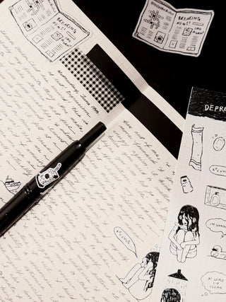 Sheet of paper with handwritten text, a pen, and printed illustrations on a black background