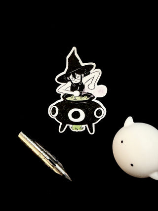 Cartoon witch in a cauldron with a pen and a small white figurine on a black background