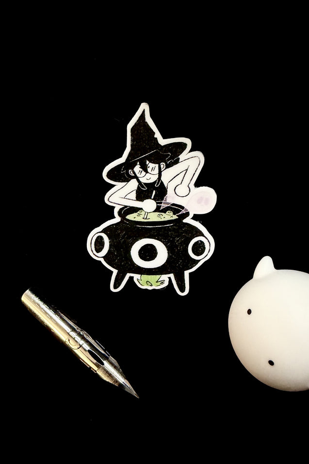 Cartoon witch in a cauldron with a pen and a small white figurine on a black background