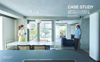 A modern interior design photograph showing people tanding in a minimalist concrete-walled room with a dining table, pendant lights, and a blue sofa.