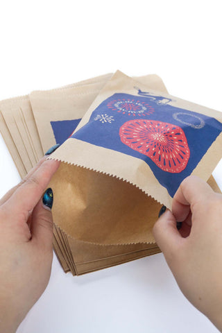 Hands holding open a small brown paper bag with colorful design.