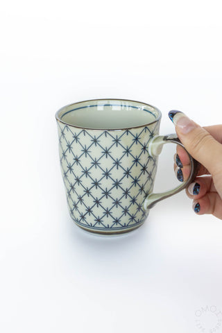 Hand holding a ceramic mug with blue geometric pattern on a white background