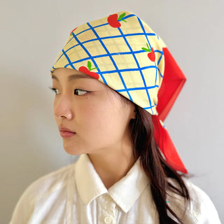 Person wearing a colorful headscarf with grid pattern and red apples on a plain background
