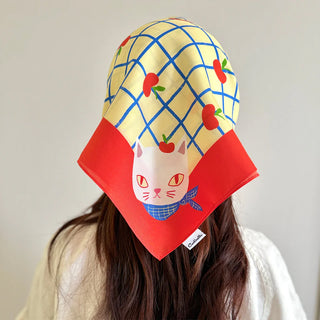 Person wearing a colorful headscarf with a cat design on a plain background