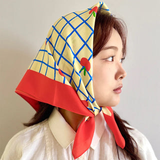 Woman wearing a colorful headscarf with a grid pattern and red accents on a plain background